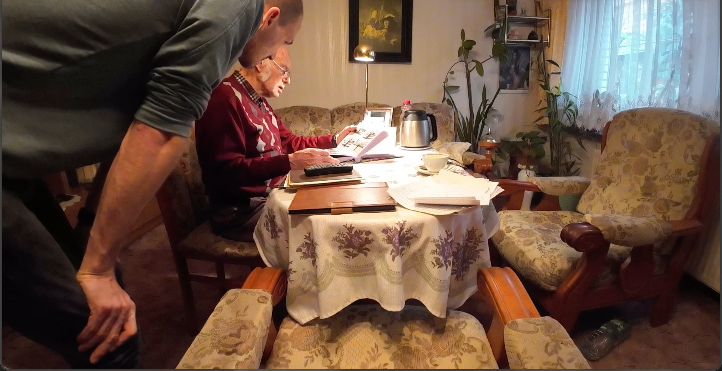 Michael und sein Opa schauen sich gemeinsam Unterlagen und Bilder am Tisch an.